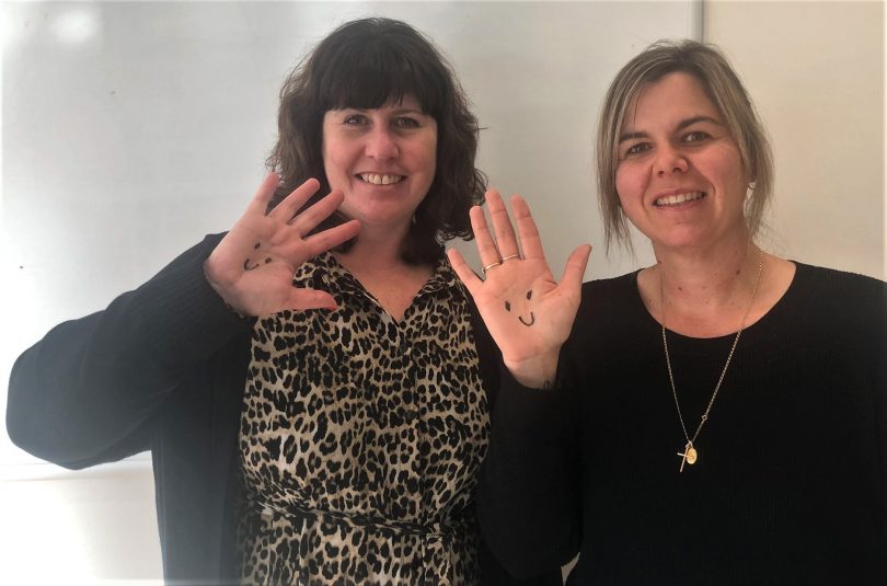 Ruth Zanker (left) and Donna Gozzard (right) hold up their hands with smiley faces drawn on them.