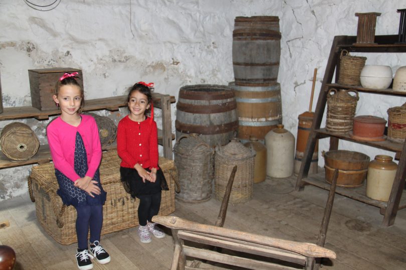 Two young girls sitting among historical barrels and baskets