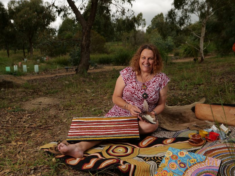 Gail Neuss sitting on ground with Indigenous artwork