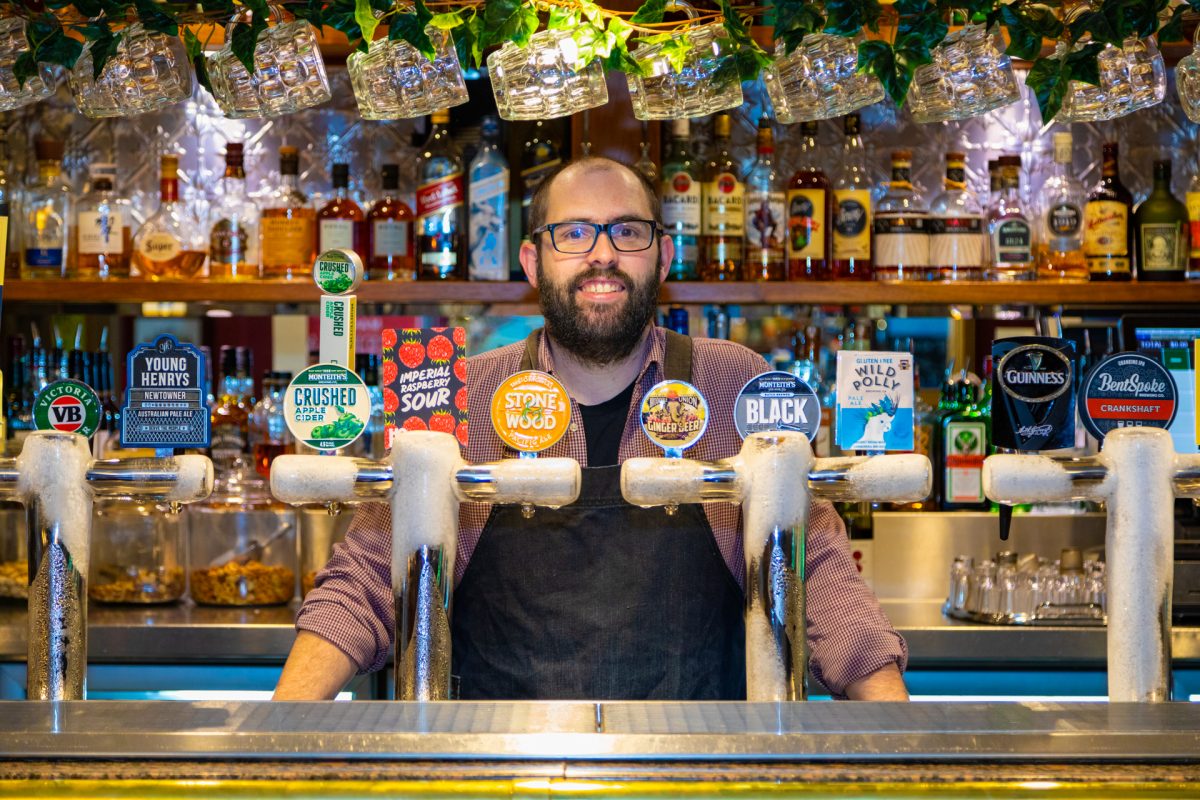 Barman standing behind row of beers.