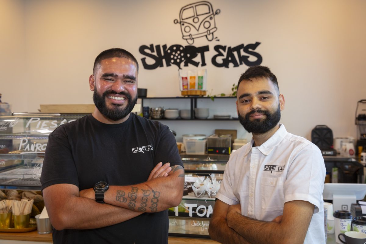 Two men smile in front of cafe logo