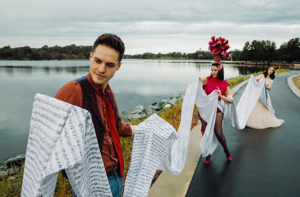 People holding fabric printed with sheet music in front of water