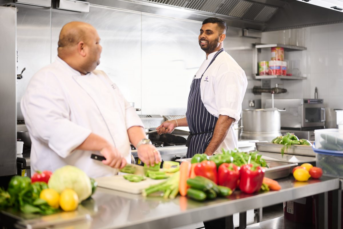 Goodwin chef Sandeep Vaid at a stove and a chef chopping vegetables
