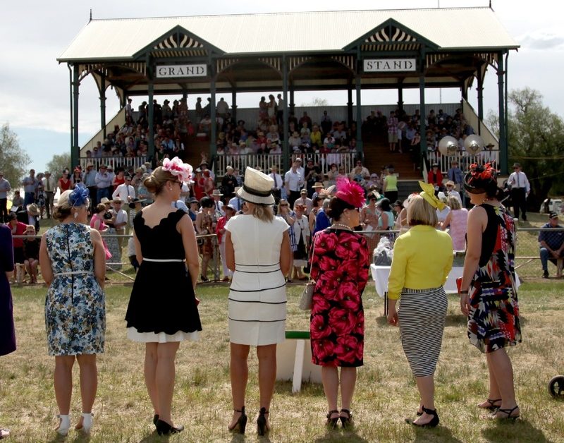 Women dressed for the races stand on the field