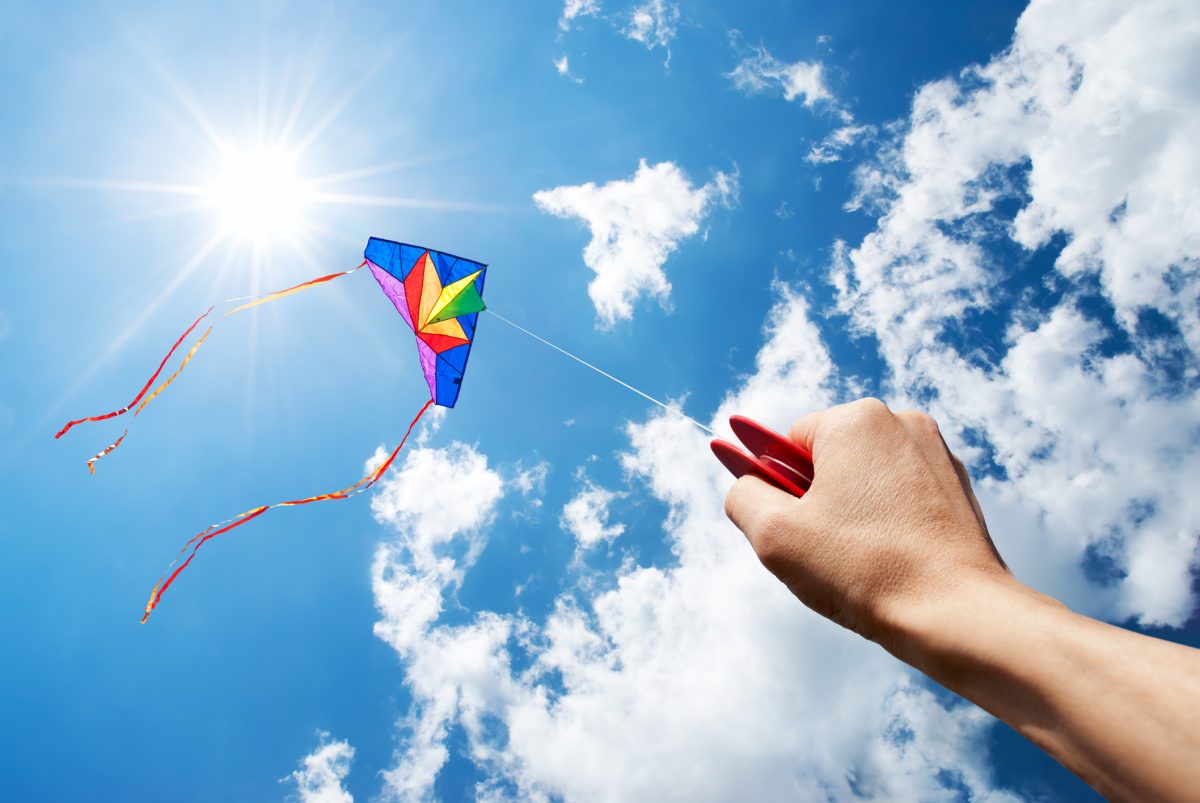 hand flying colourful kite in a blue sky