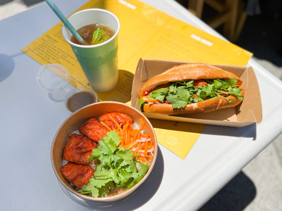 bowl of rice with toppings, banh mi roll with fillings, and iced drink in takeaway cup
