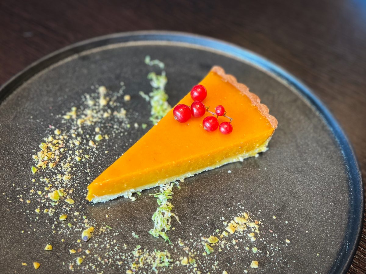 A slice of a bright orange tart with red berries on top.