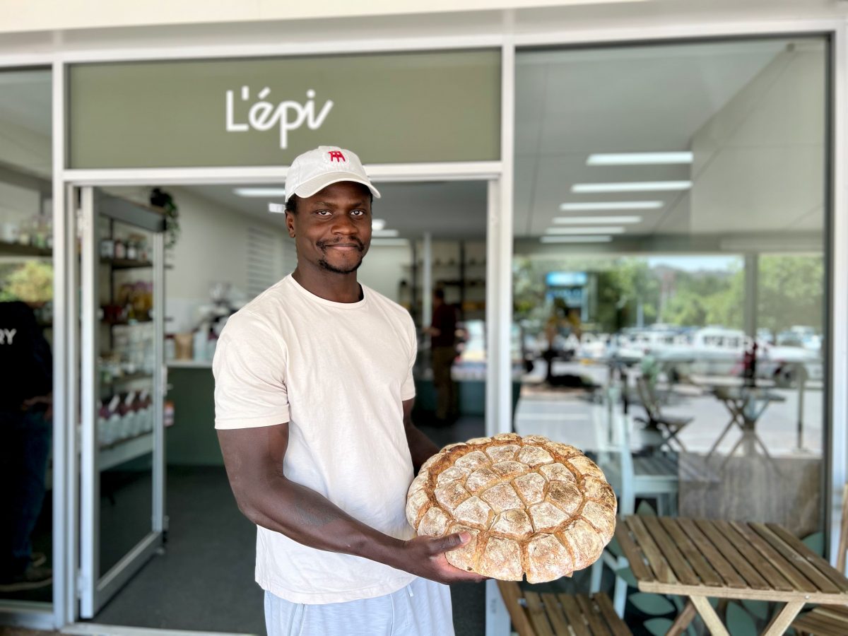man holding large wheel of bread outside L'epi Bakery