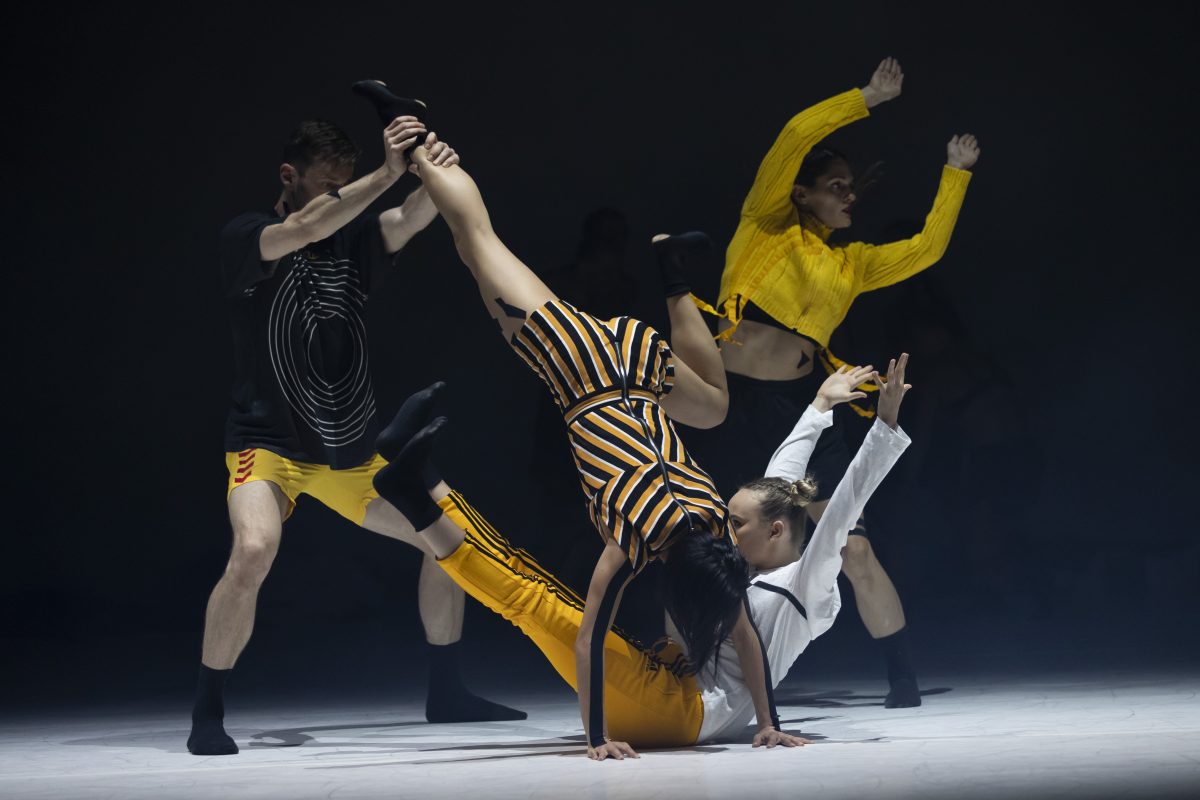 dancers from Sydney Dance Company in black and yellow costumes performing on stage