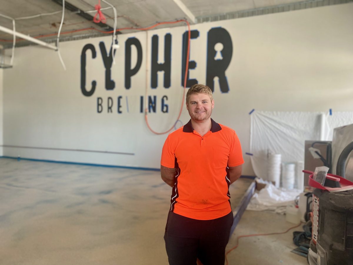 Jeff wears high vis and smiles in front of the Cypher Brewing sign in a construction site