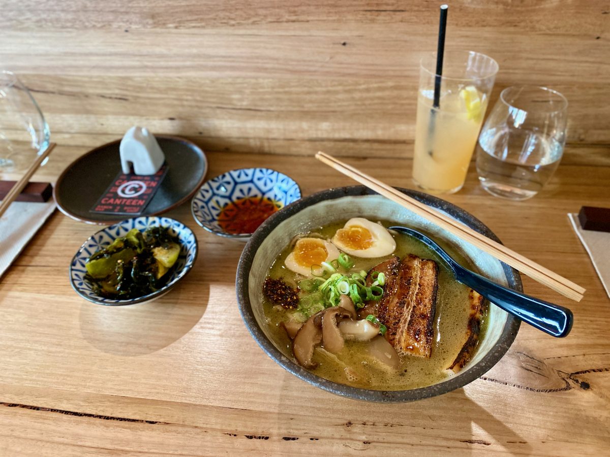 Bowl of Ramen with condiments on wooden bench at Canteen