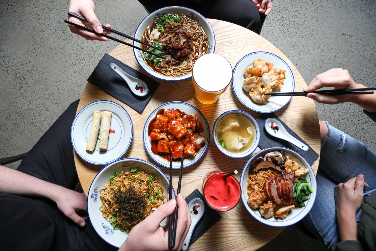 many delicious looking dishes on a table with hands holding chopsticks