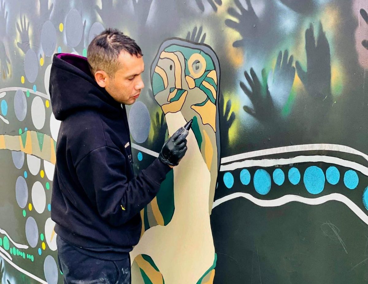 man painting mural with goanna design