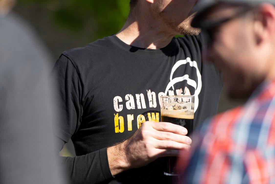 Person wearing Canberra brewers logo on Tshirt and holding half-drunk beer