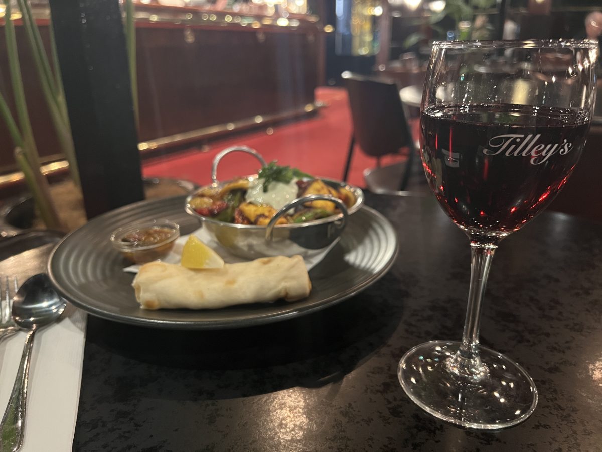 A glass of wine to the right and plate with curry on the left