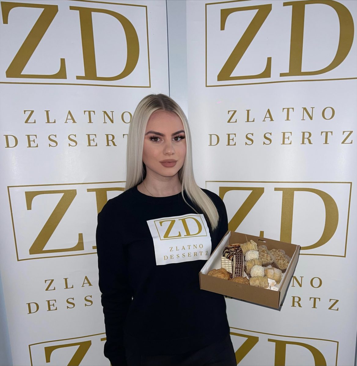 Woman holds box of sweets in front of logo