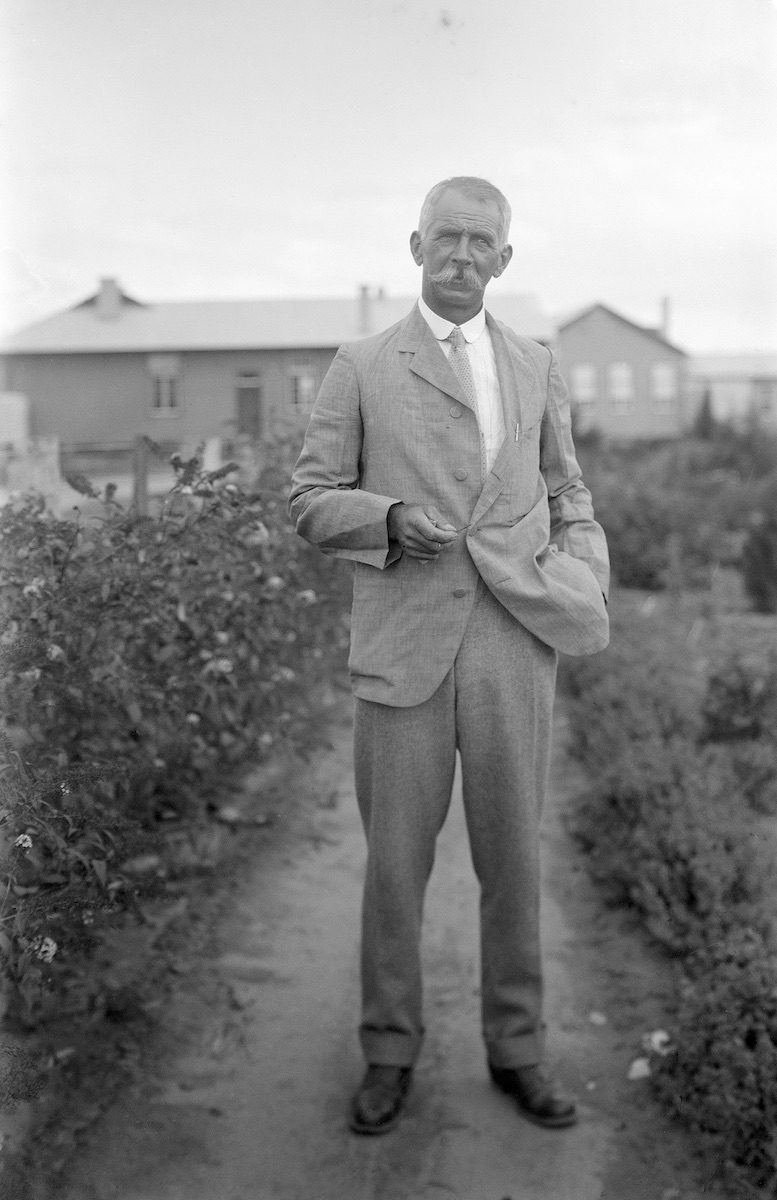 Charles Weston is pictured at Yarralumla Nursery, standing near lots of bushes. He is wearing a suit and he has a bushy moustache. Circa 1920s.