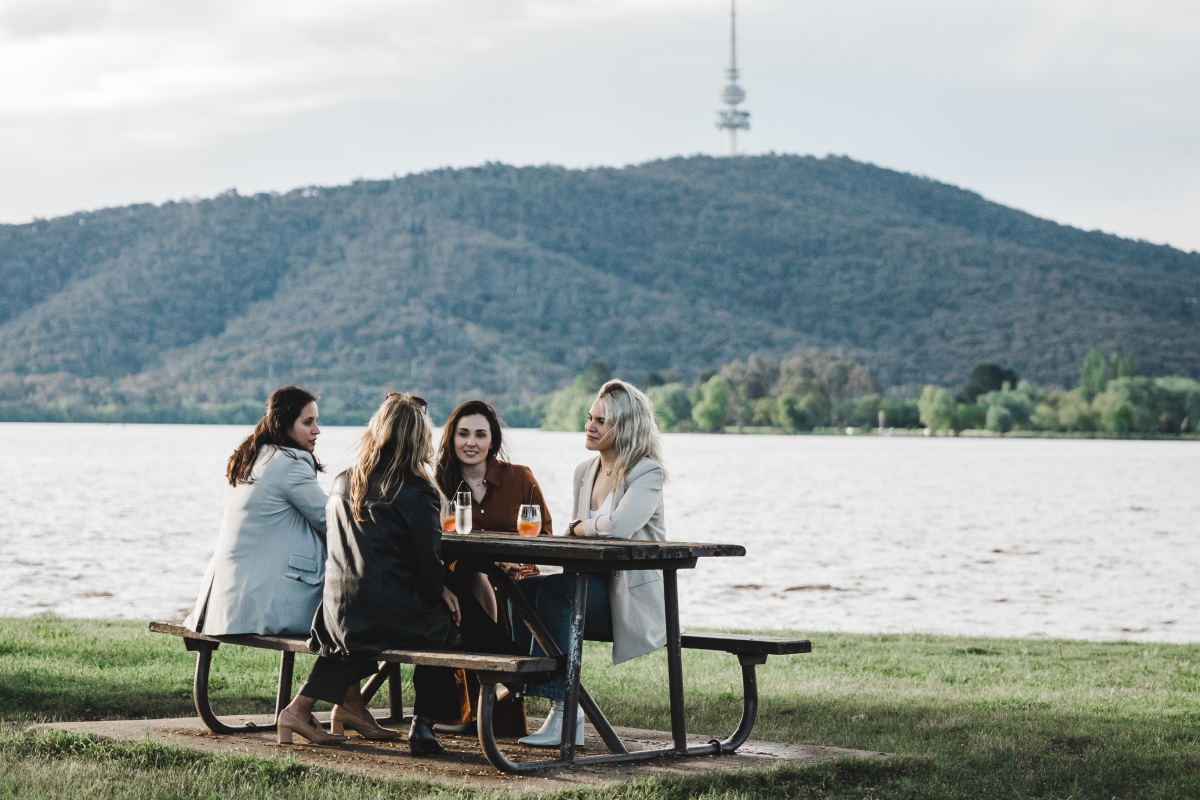 four people sitting on a picnic table outside by the water