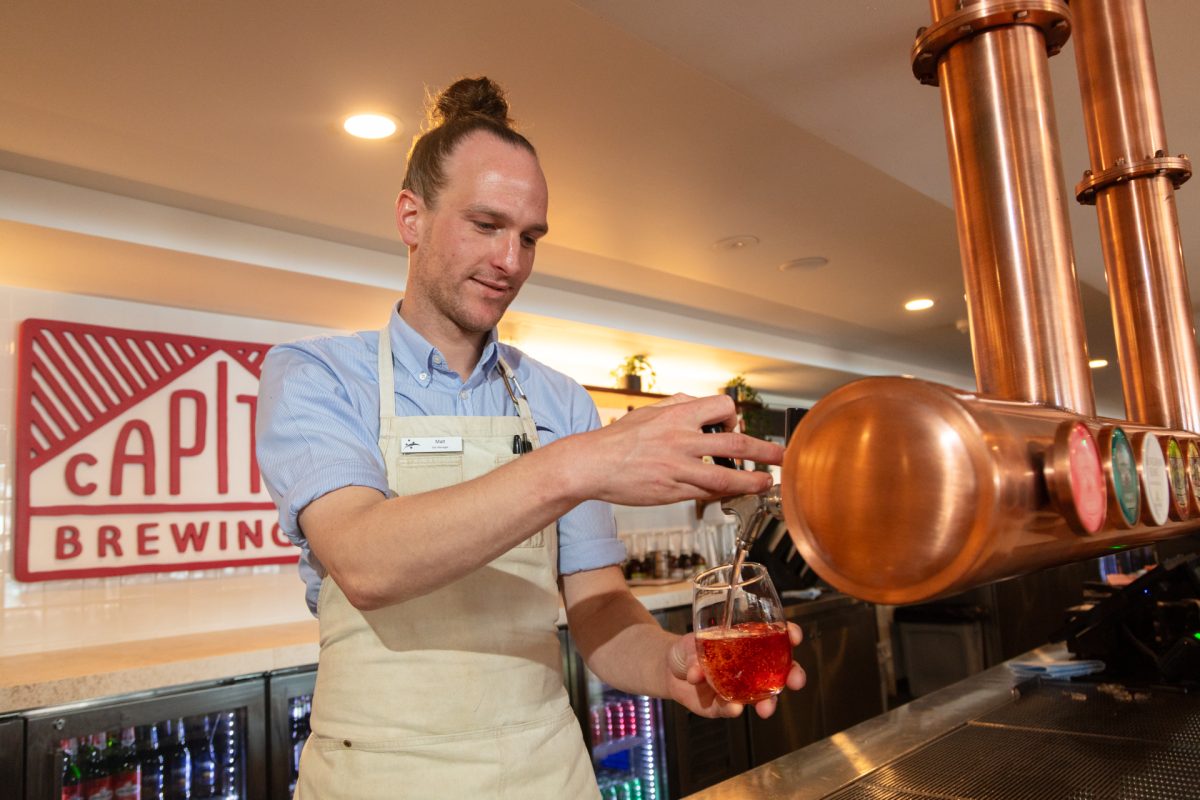 A man in apron and top-knot pouring a drink