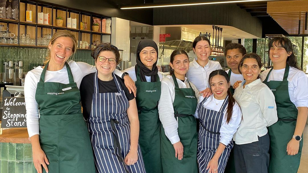 Group of women in aprons smiling in front of cafe counter