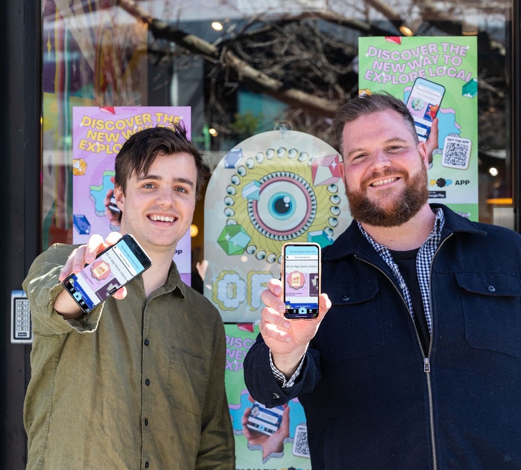 two men holding phones with POP Canberra apps on the screens