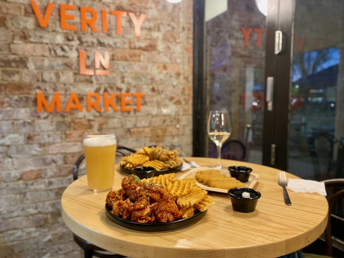 A table with dishes of fried chicken in front of a Verity Ln Market sign on a brick wall
