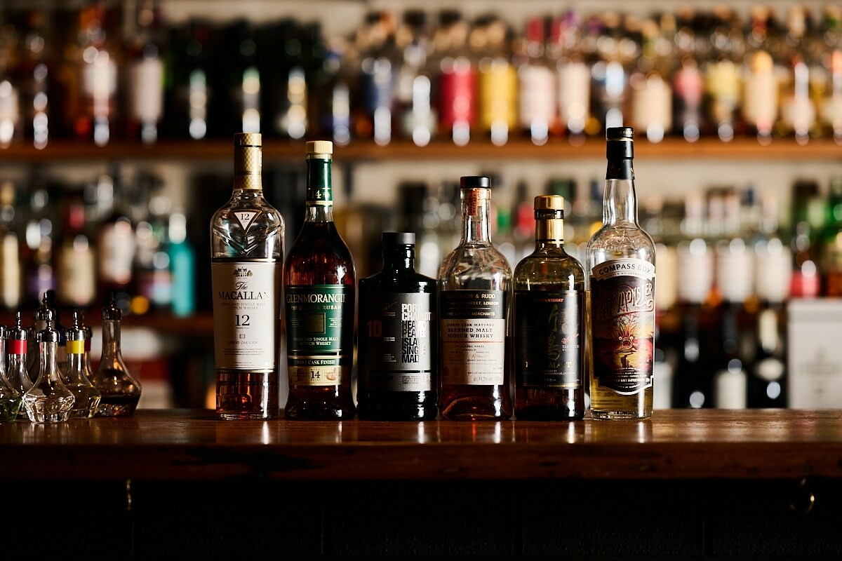 A row of whisky bottles on a bar in front of shelving with other alcohol 