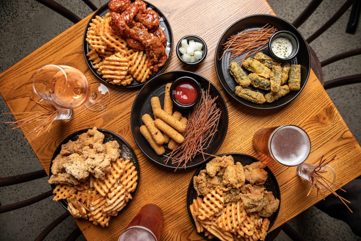 A table with multiple plates of fried chicken, waffle fries, chips and glasses of beer.