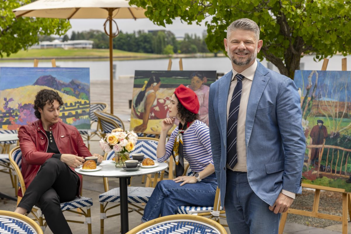 Dr Nick Mitzevich in an outdoor cafe scene with paintings at the launch of the NGA's major exhibition for 2024 featuring the work of post-Impressionist artist Paul Gauguin. 