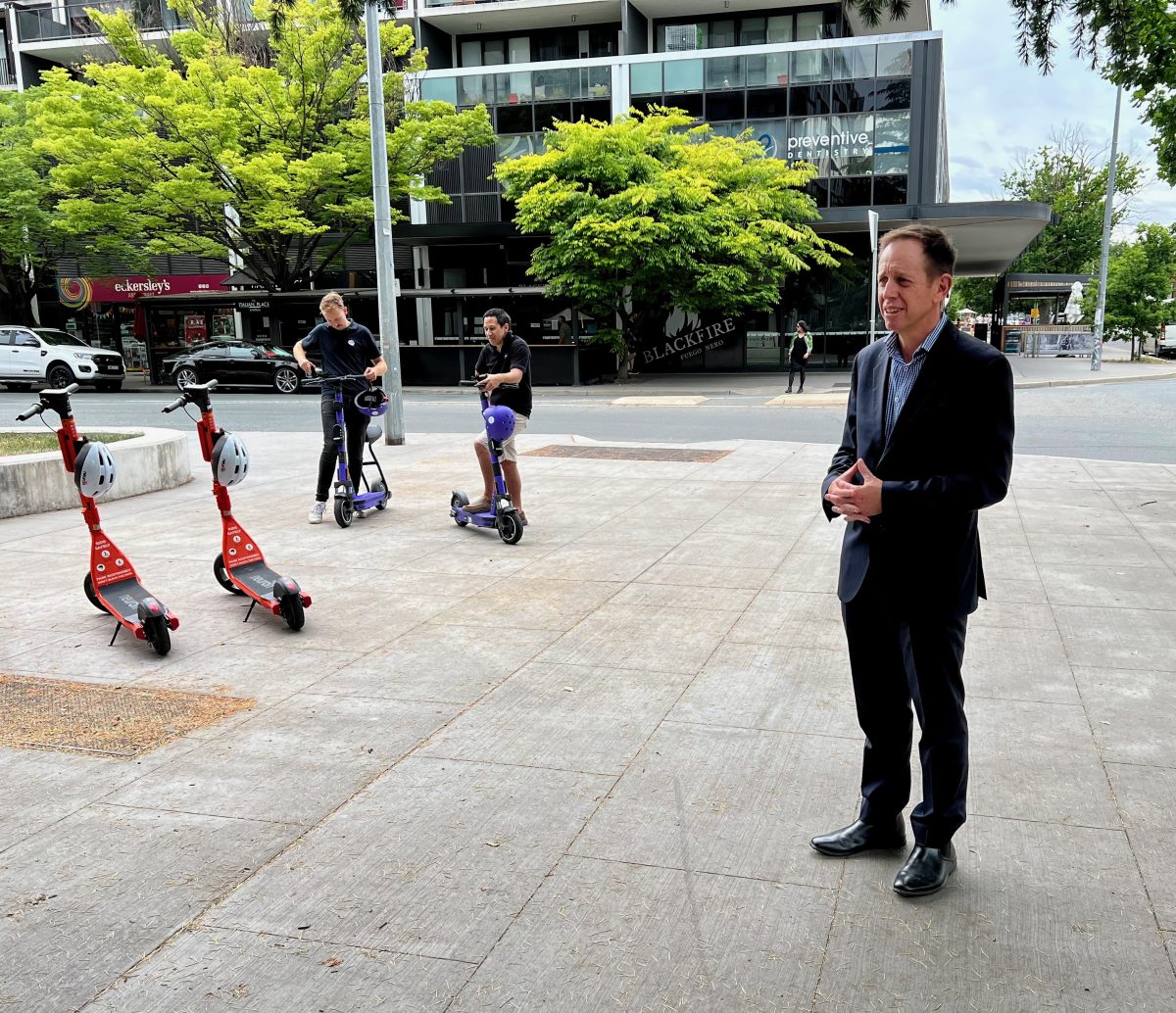 Shane Rattenbury stands in front of electric scooters