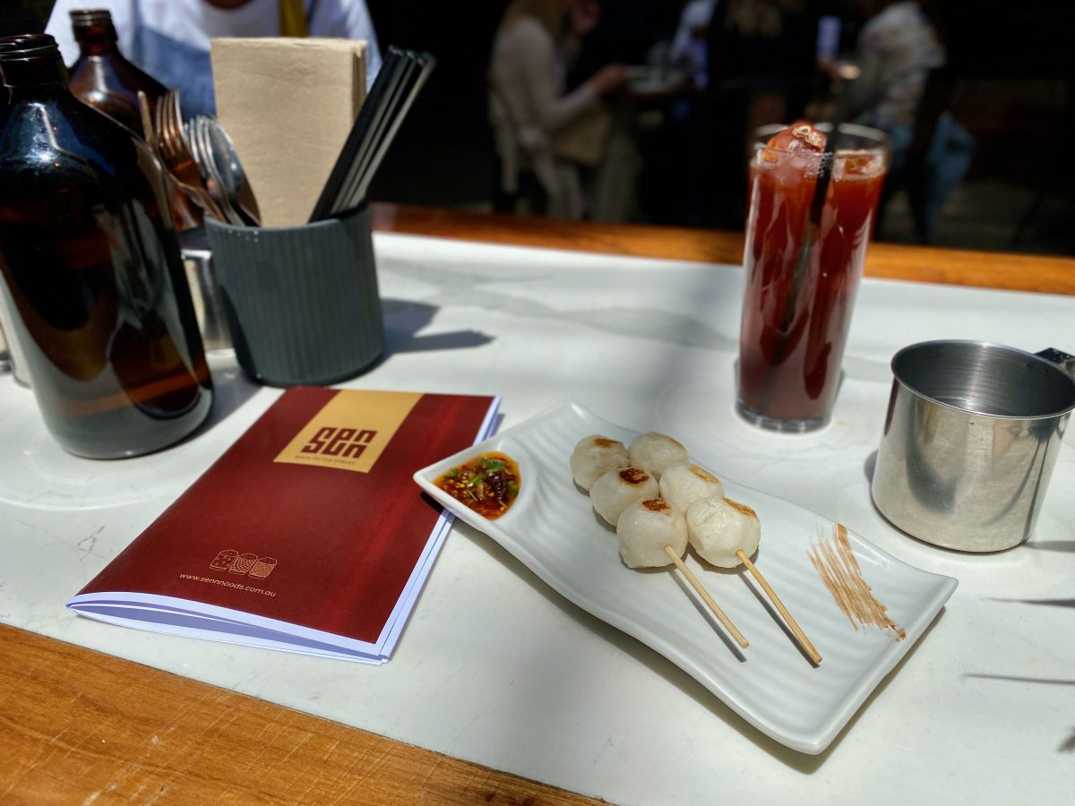 Two skewers with three grilled fish balls each on a rectangular plate with a section holding chilli oil.