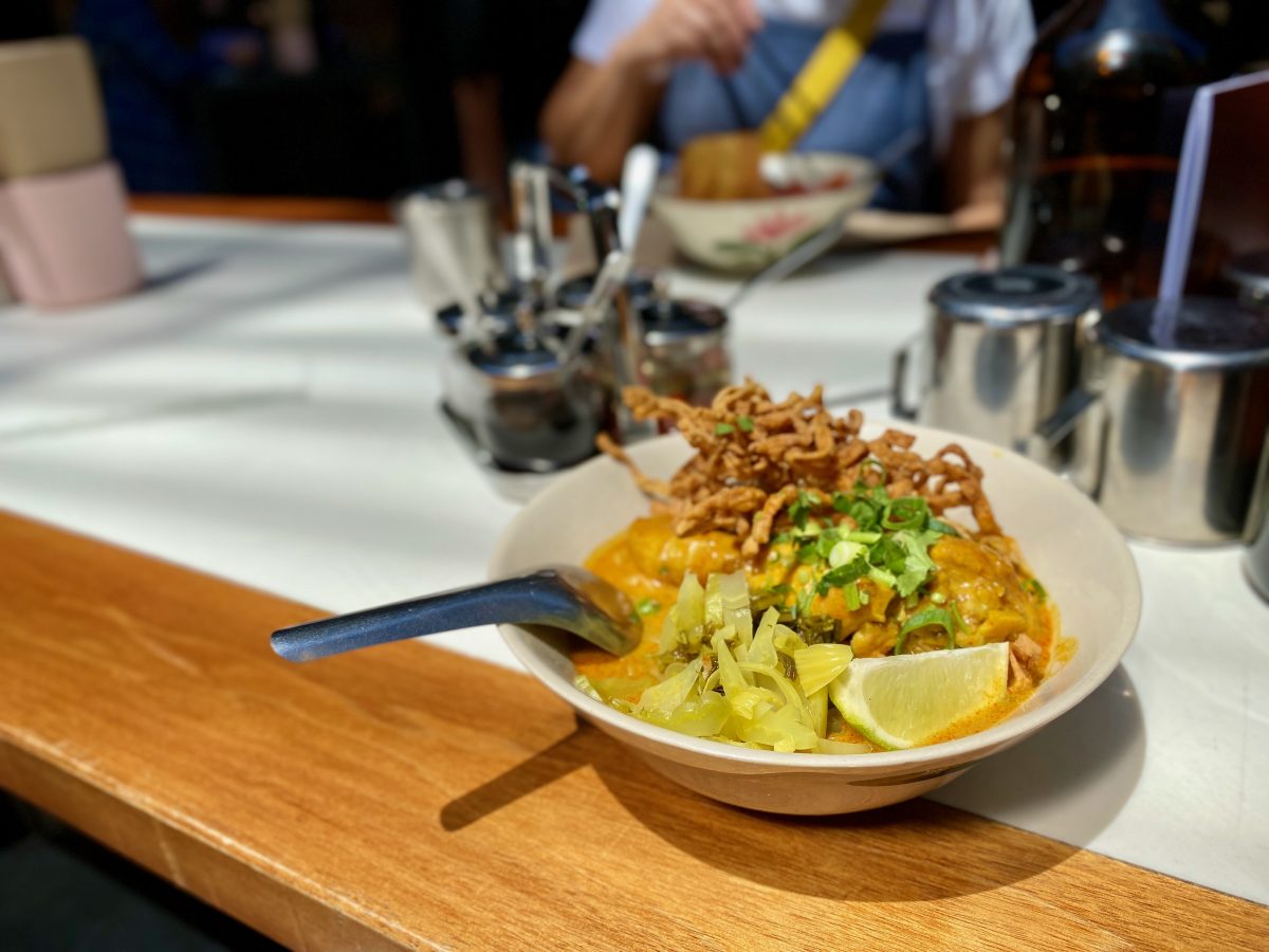 A bowl of Thai dish Khao Soi Gai topped with crispy noodles anda a wedge of lime. 