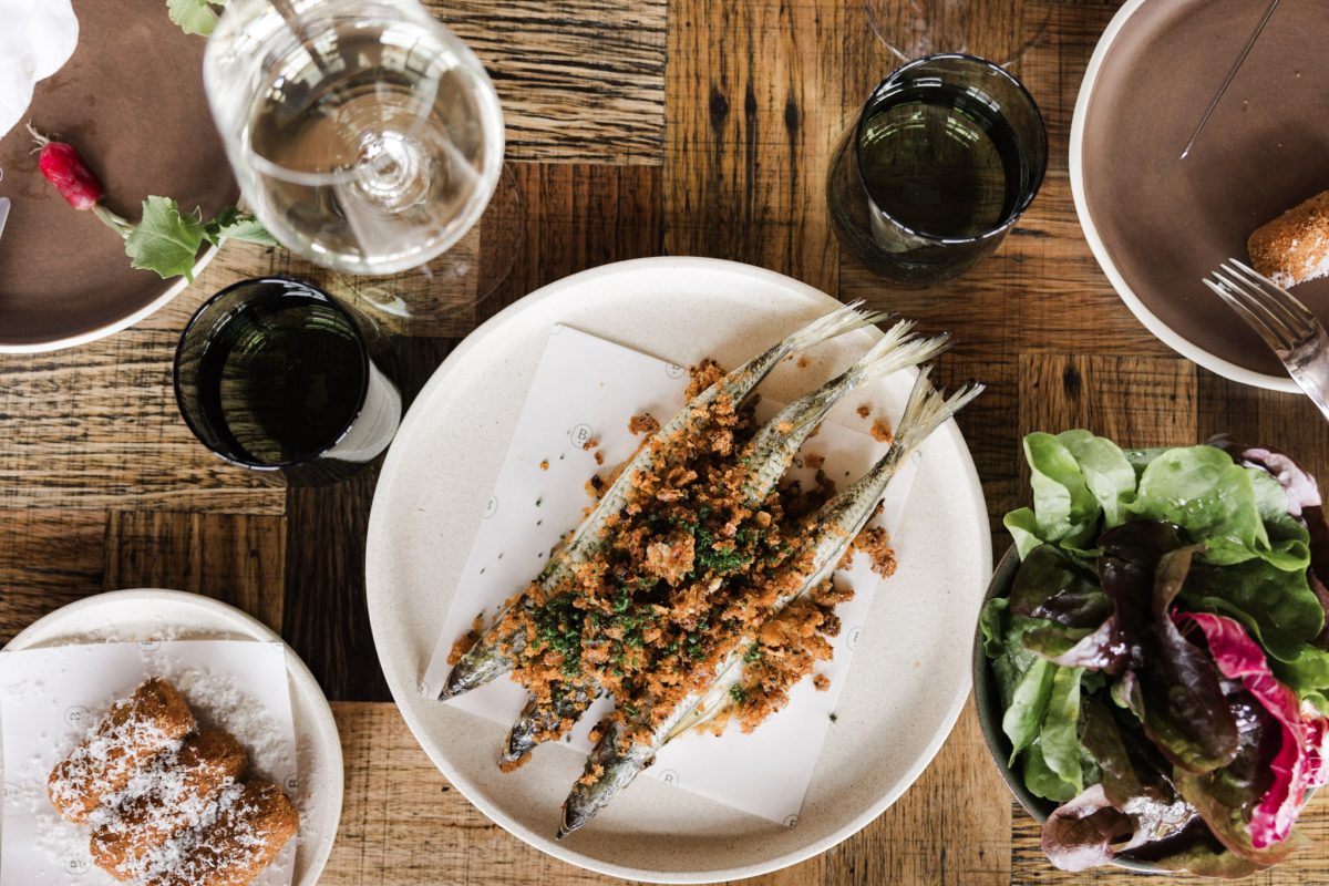 Plate of small fish with breadcrumbs on table set with wineglasses