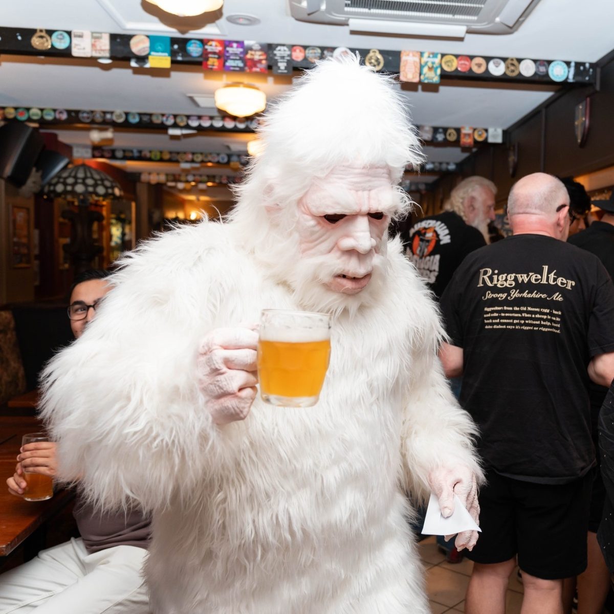 Someone in a white yeti costume holds a pint of beer.