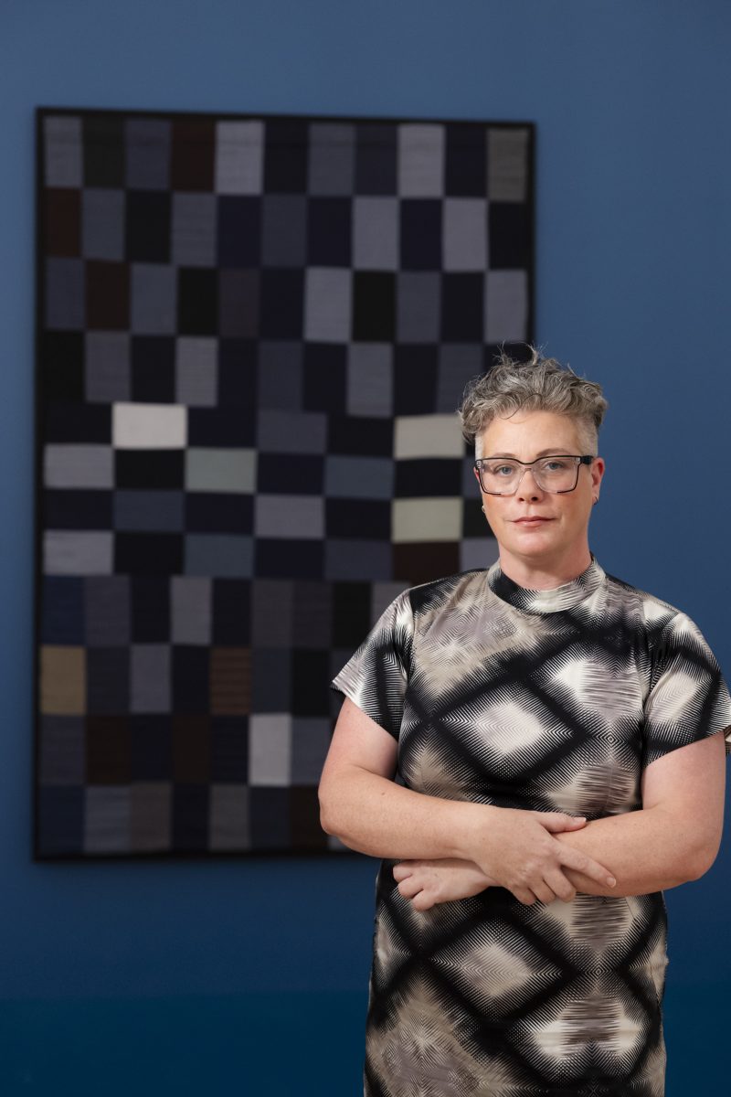 Woman with arms folded in front of wall hanging.
