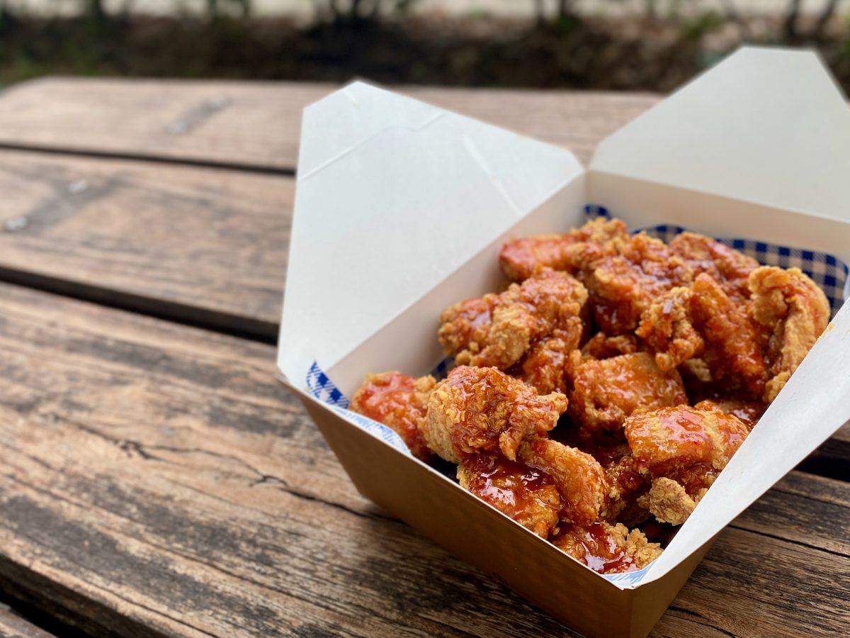 A large takeaway box of Korean fried chicken with shiny sauce coating.