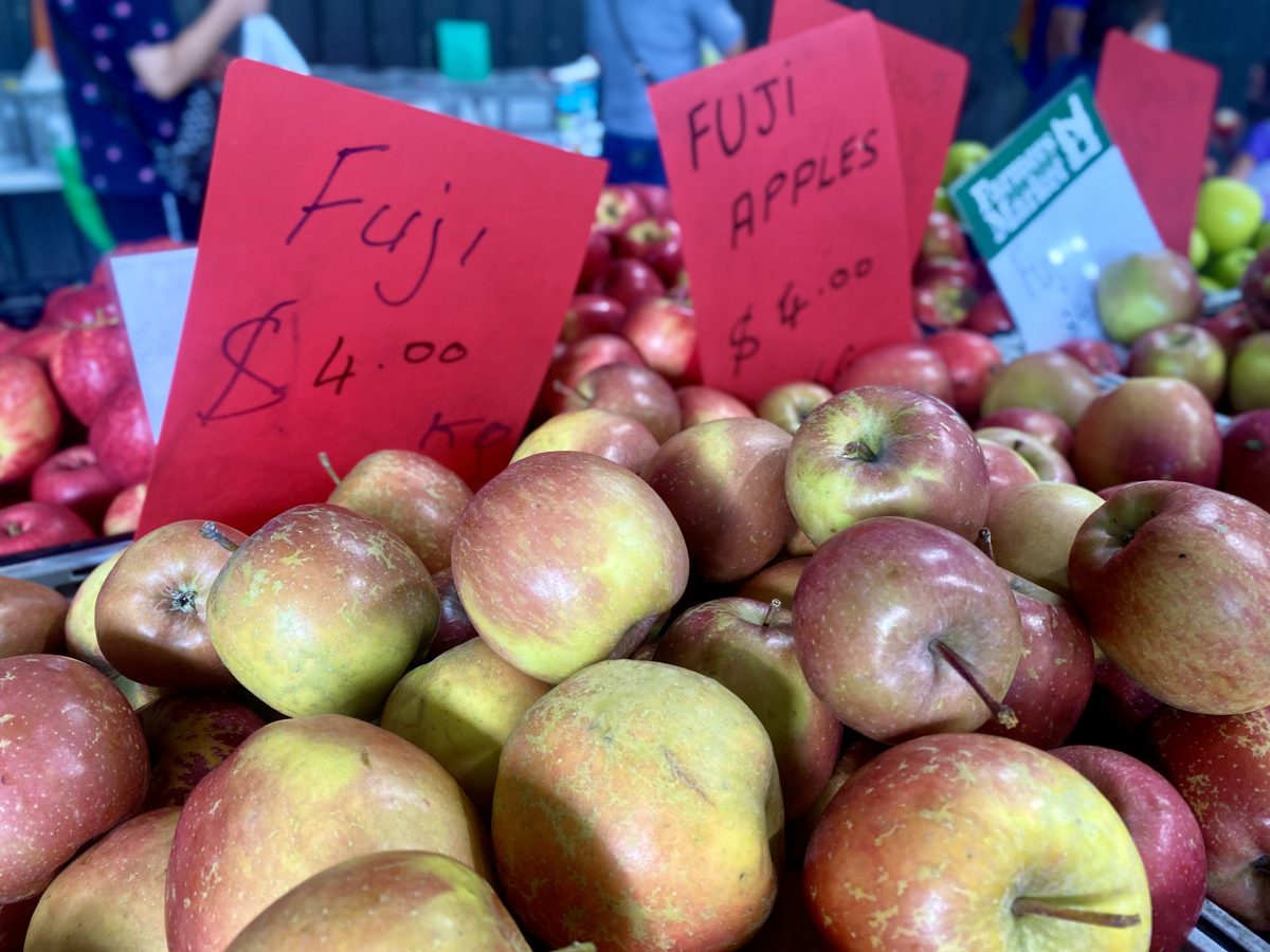 A red sign reading 'Fuji $4.00 kilo' with fresh apples.