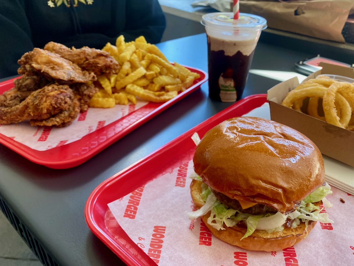 Burger and fried chicken with chips on two red trays, with a chocolate milkshake. 