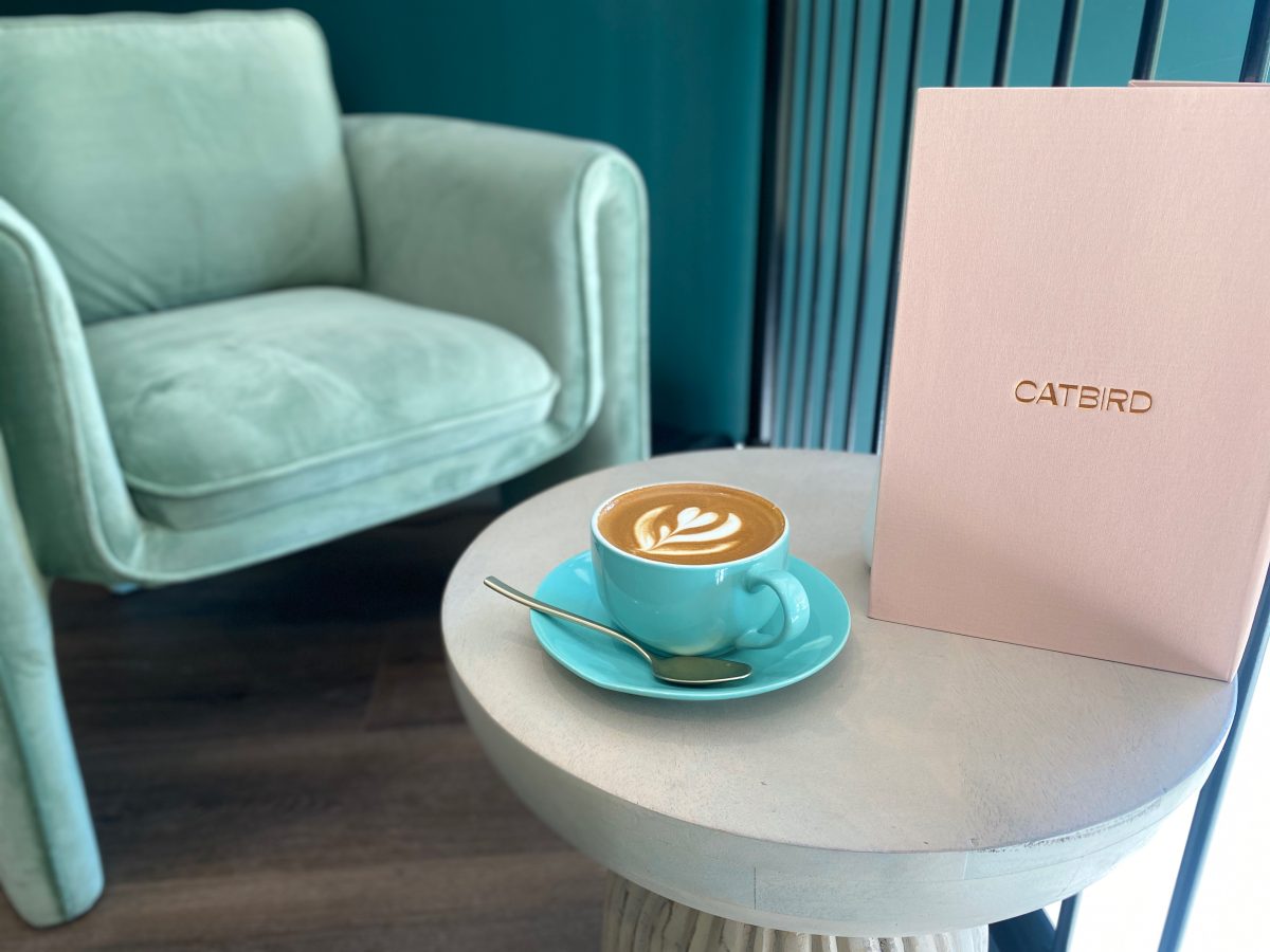 Coffee in aqua coloured cup next to pink menu with Catbird logo