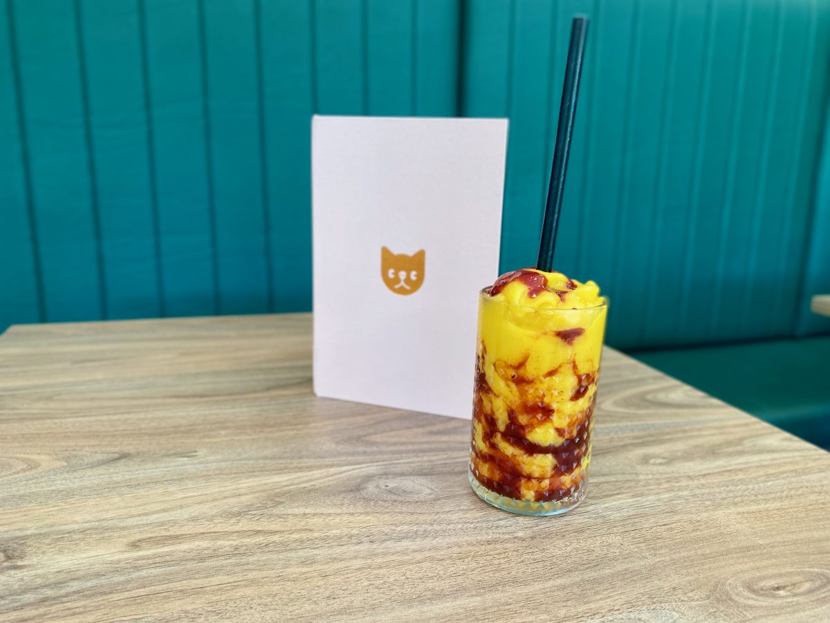 Mango smoothie with chilli sauce in front of pink menu with Catbird logo.