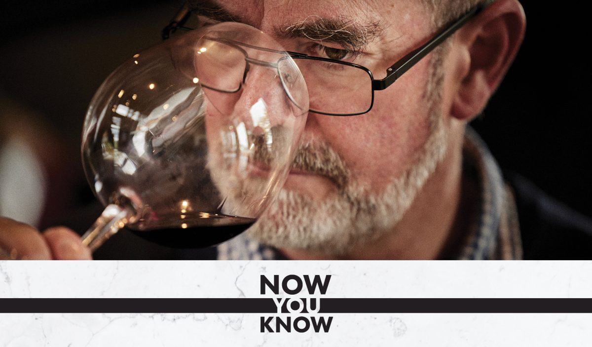 Tim smells a glass of red wine. A black and white banner reading 'Now You Know' is overlaid on the photo. 