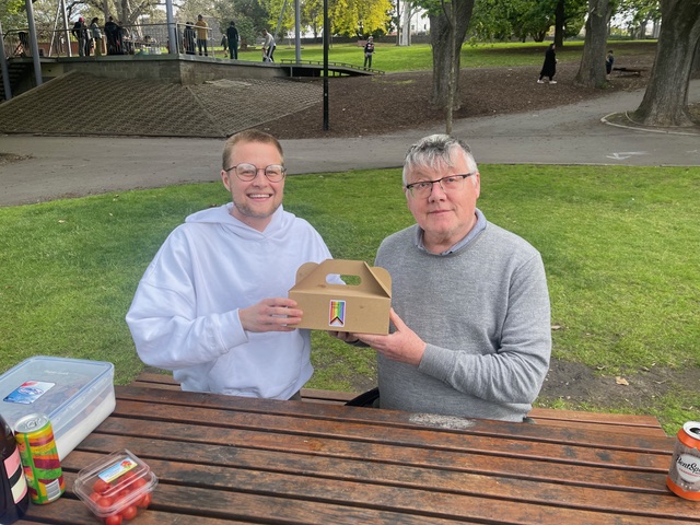 Andy and Graham hold a catering box with Queer Food logo