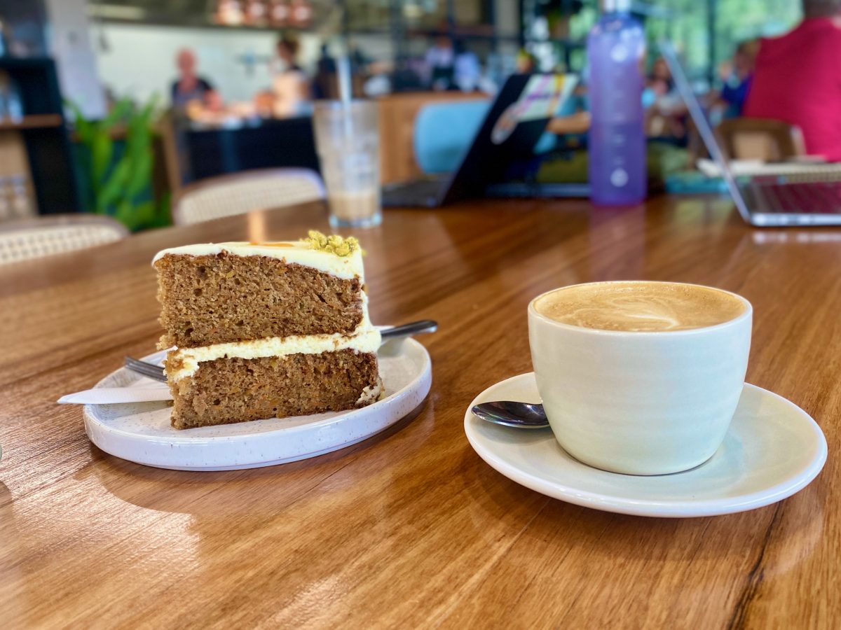 Delicious looking two-tiered carrot cake with frosting and a cup of coffee.
