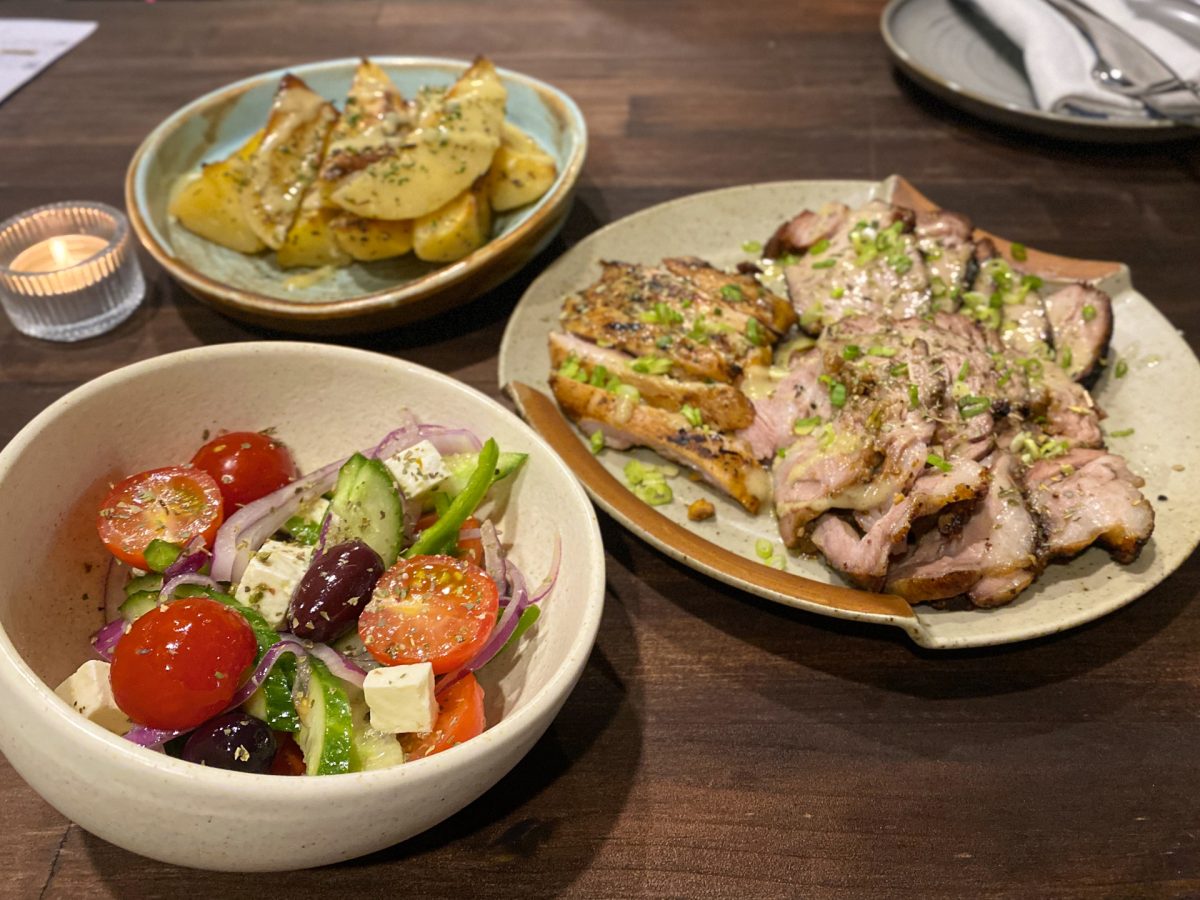 A bowl of greek salad, plate of sliced, roast meats and a bowl of roast potatoes with herbs