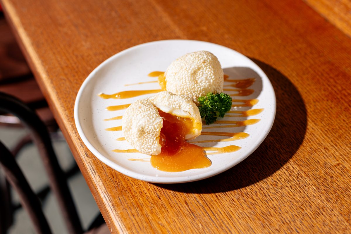 Two sesame balls on a plate, one has been split open to reveal a gooey pumpkin filling.