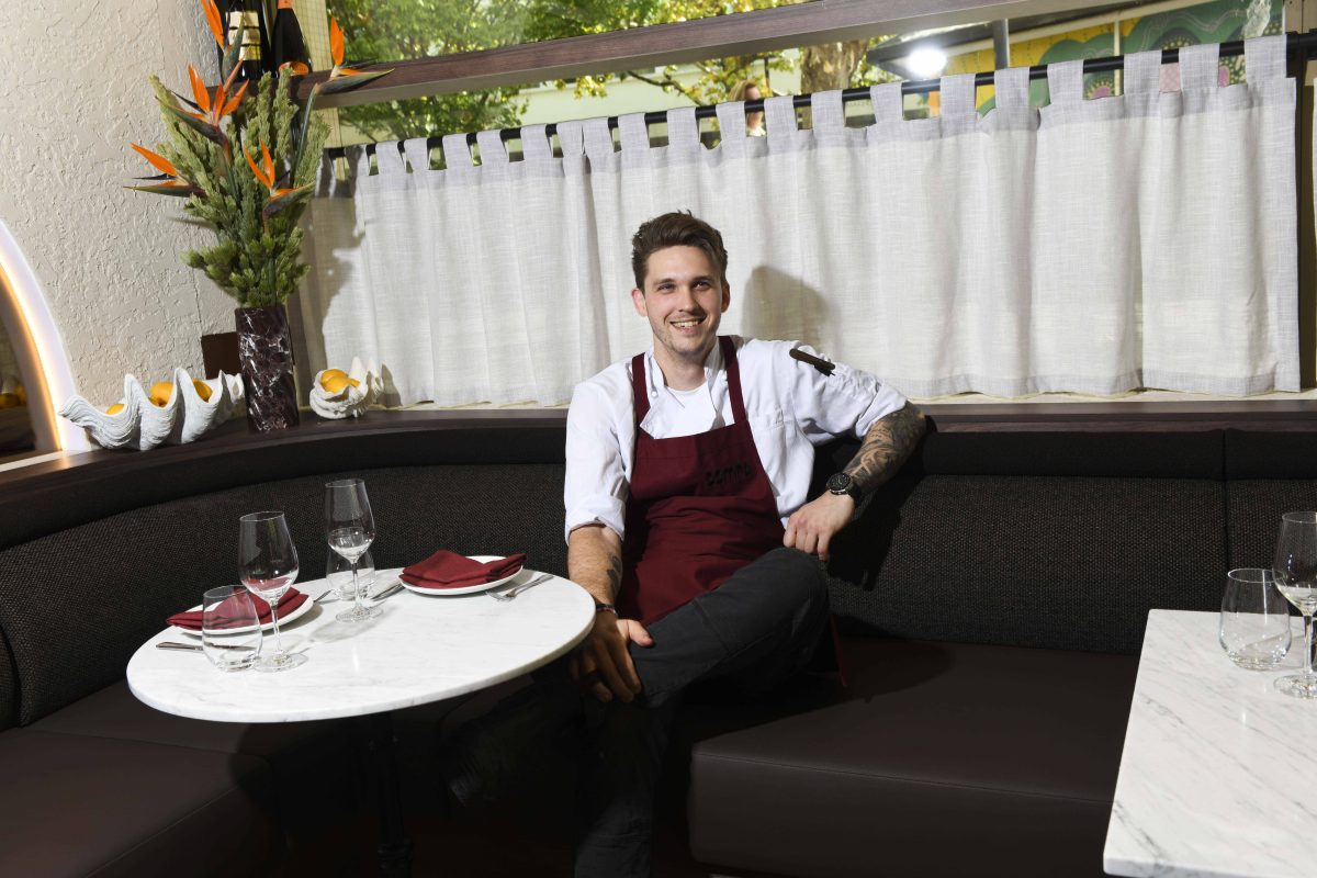 Chef Nick Mathieson in white shirt, red apron, sitting in restaurant