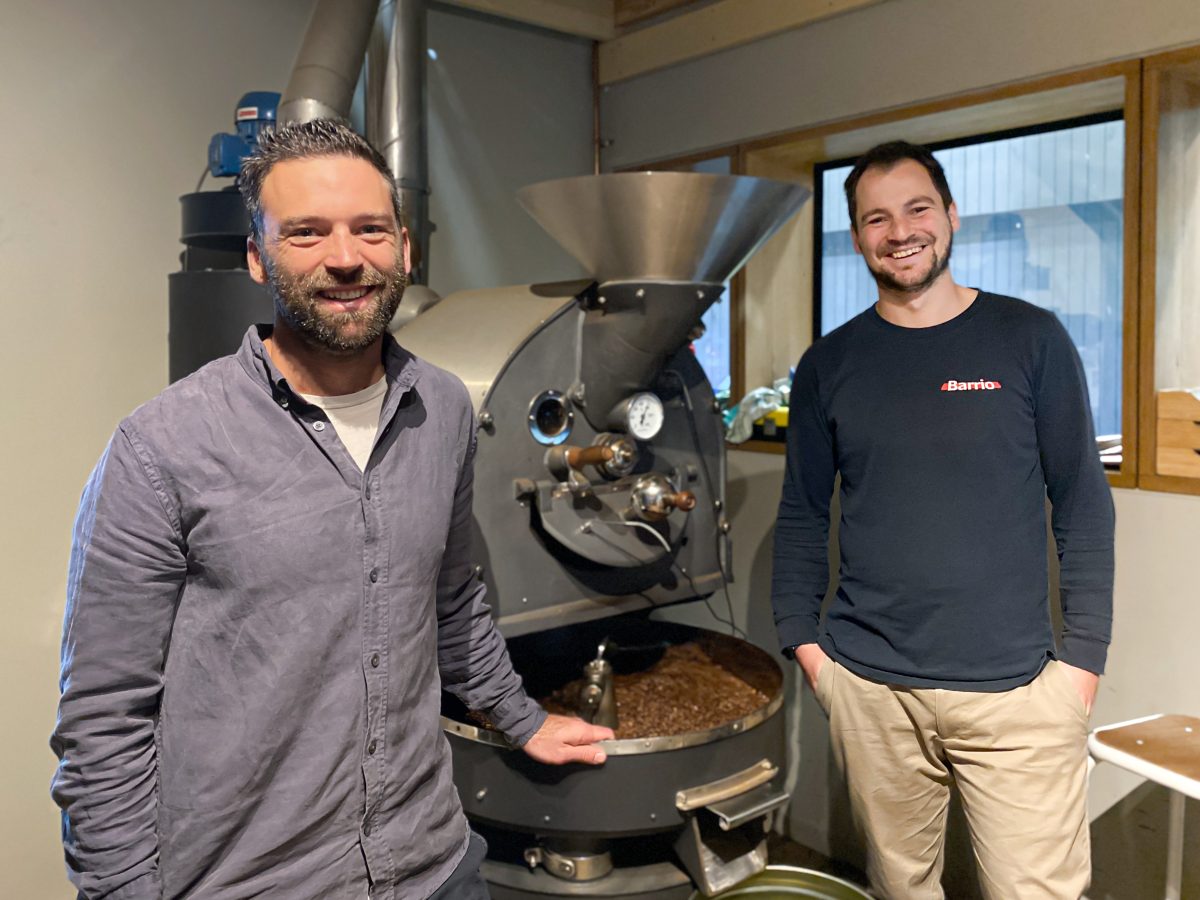 Sam Burns and Max Neve stand next to coffee roaster