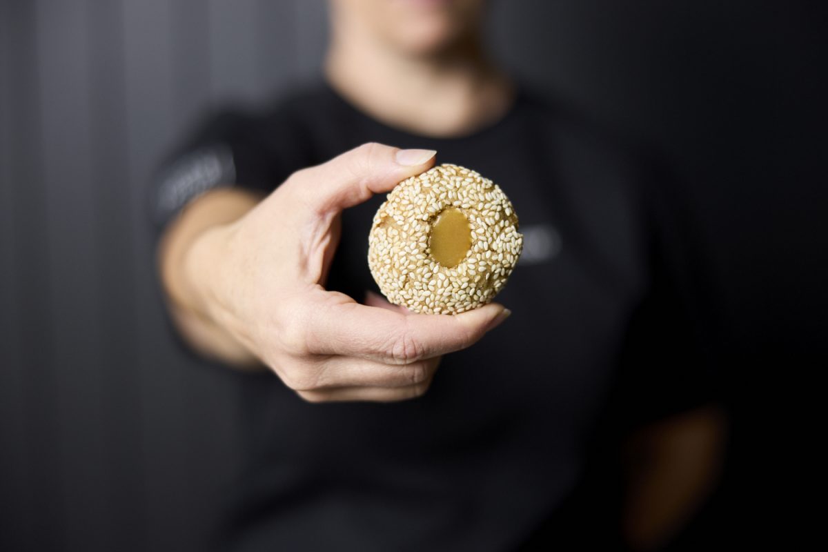Hand holds a sesame seed-encrusted biscuit with butterscotch centre against a black background