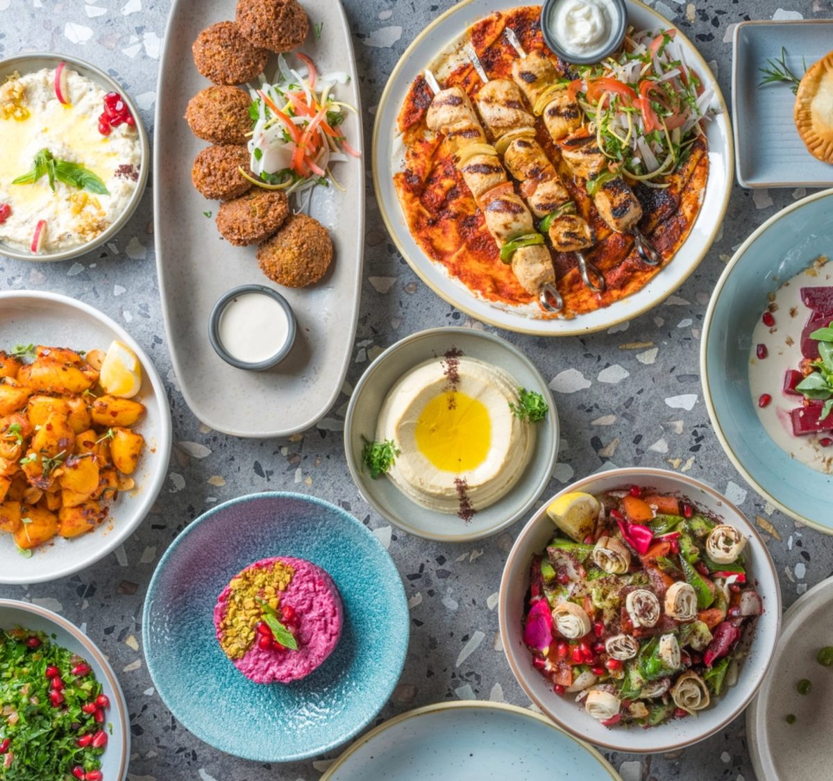 A table laden with middle eastern dishes like dips and meat skewers