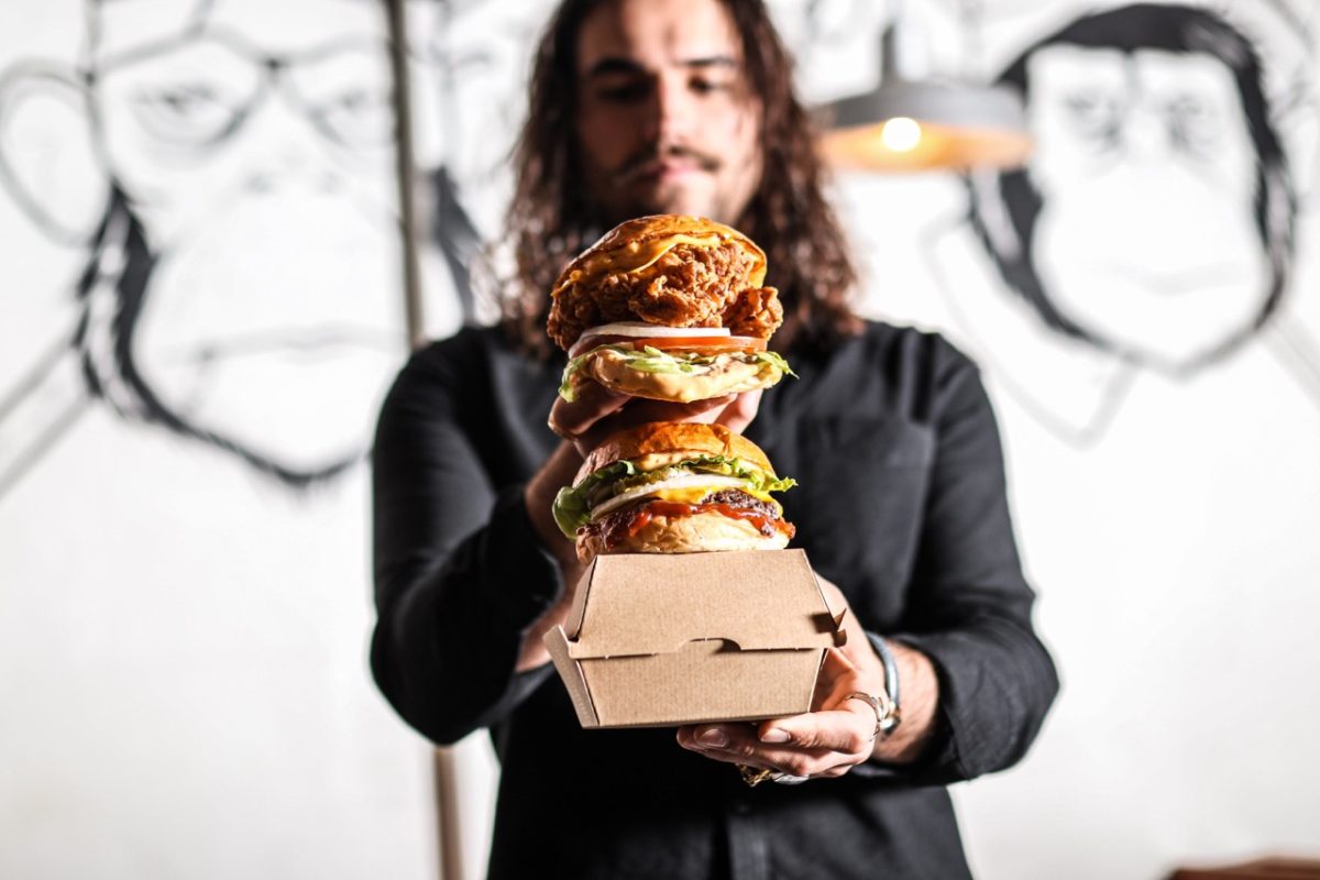 Man with long hair holds stack of burgers